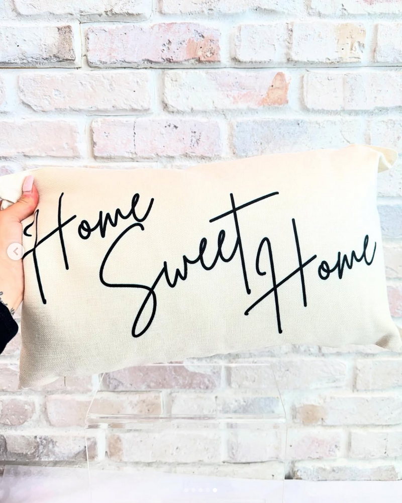 Pillow with 'Home Sweet Home' text held against a brick wall.